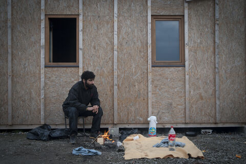  The Grande Synthe camp, the only humanitarian camp in France, a few days from the first year of its opening (March 7, 2017). Open following the closure of the Jungle in Calais to welcome migrants. Man warming is hands next to the infomation desk. Grande Synthe. 2017.