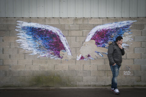 The Grande Synthe camp, the only humanitarian camp in France, a few days from the first year of its opening (March 7, 2017). Open following the closure of the Jungle in Calais to welcome migrants. A man is standing in front of a drawing showing a pair of wings. Grande Synthe. France. 2017